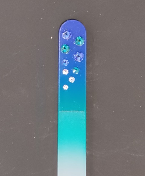 Nagelvijl met blauwe Swarovski steentjes op een blauw/groene achtergrond