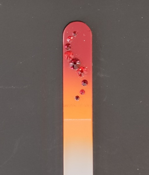 Nagelvijl met rode Swarovski steentjes op een rood/oranje achtergrond